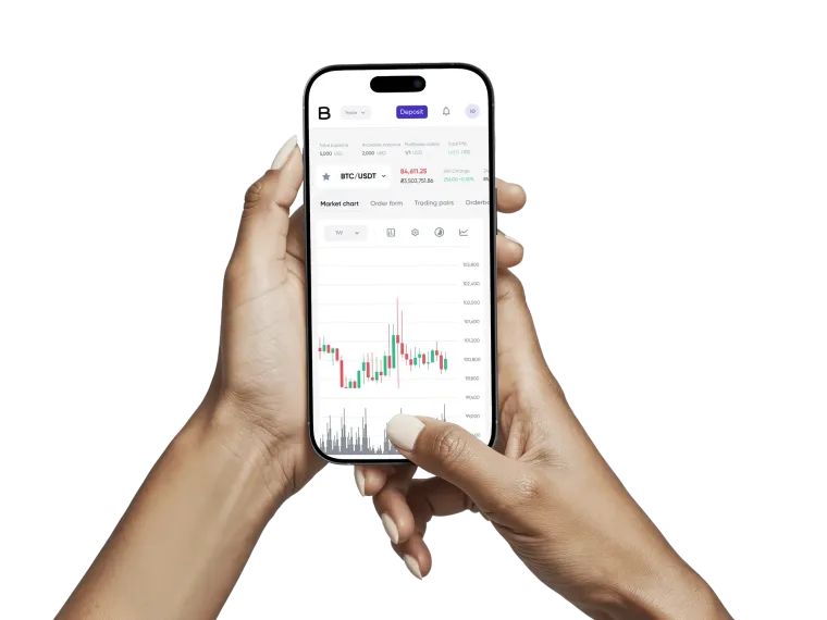A phone held in one hand, showing the BTC/USDT price with its daily figures above a candlestick chart.